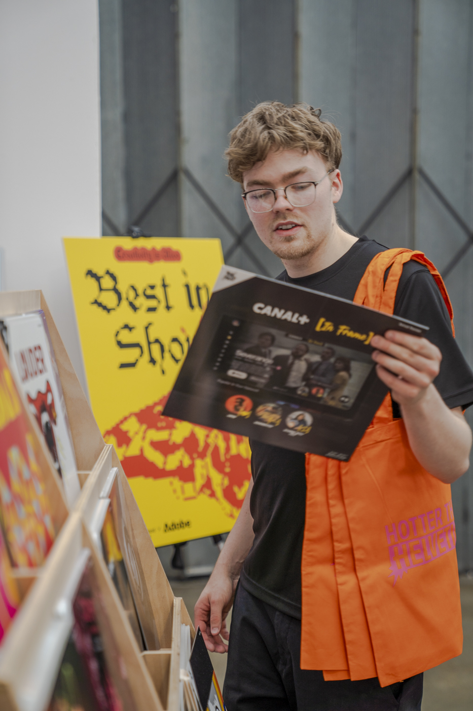 A person browses vinyl records, holding a Canal+ magazine beside a yellow 'Best in Show' sign.