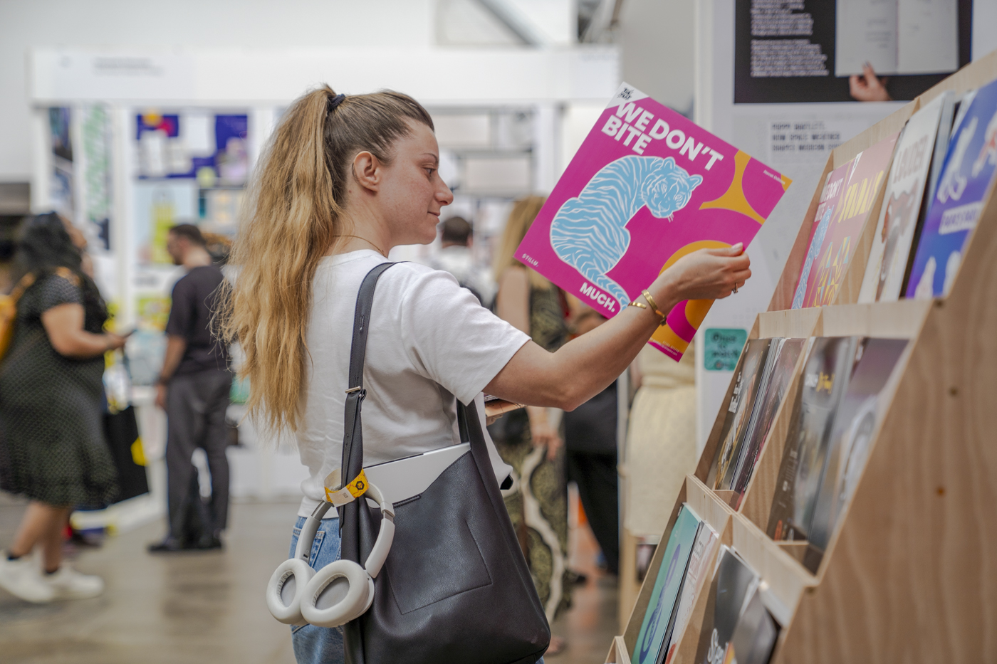 A young person with a ponytail browses vinyl records at a display stand in an indoor market or shop.