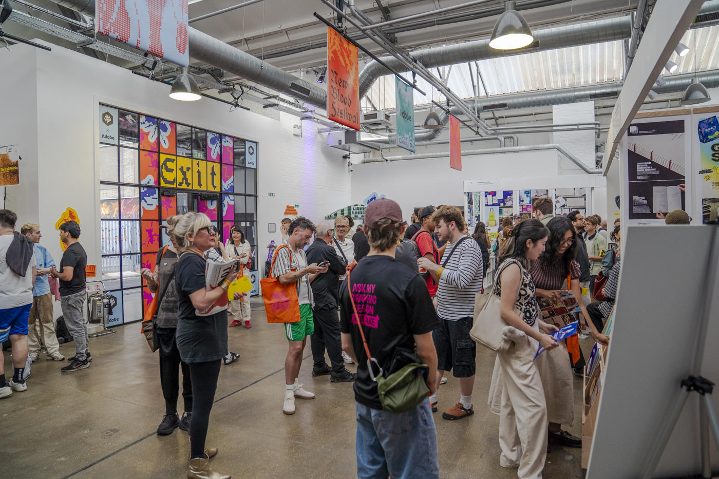 A group of people stands in an exhibition hall with colourful wall art, hanging banners and exposed ceiling beams.