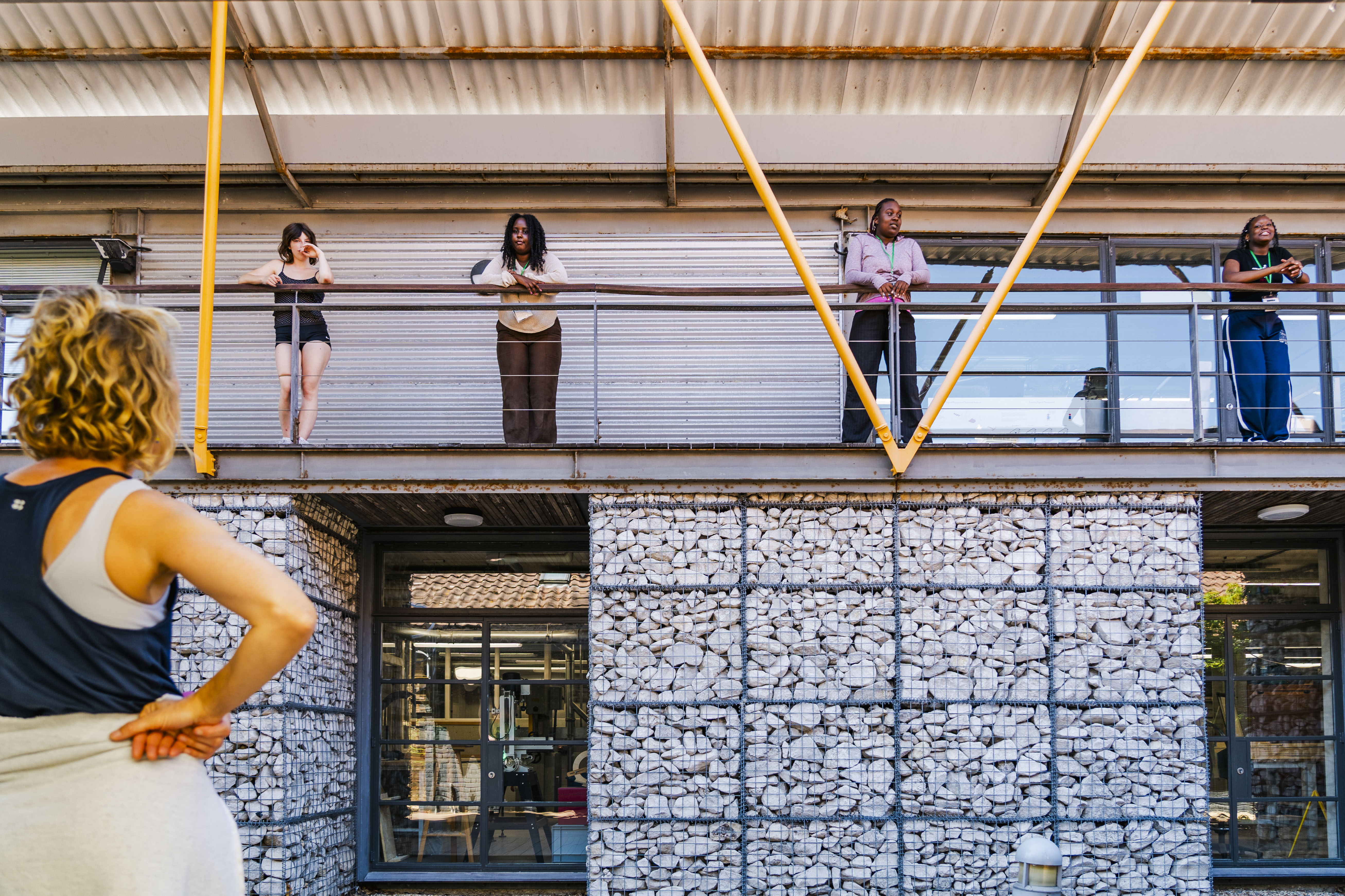 dance teacher giving feedback to 4 female dance students standing on first floor outdoor balcony