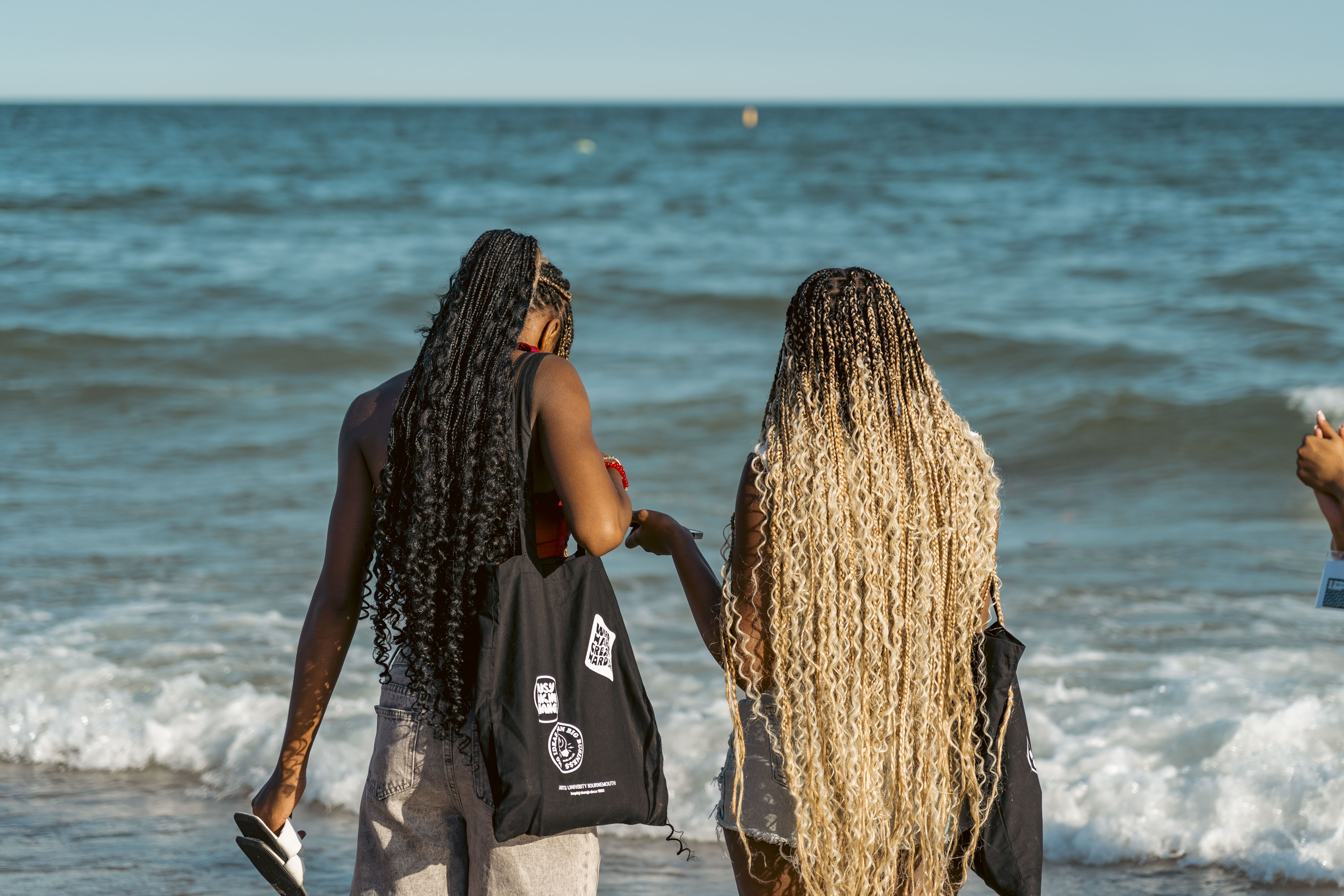 two females on the beach walking into the sea with their backs to camera
