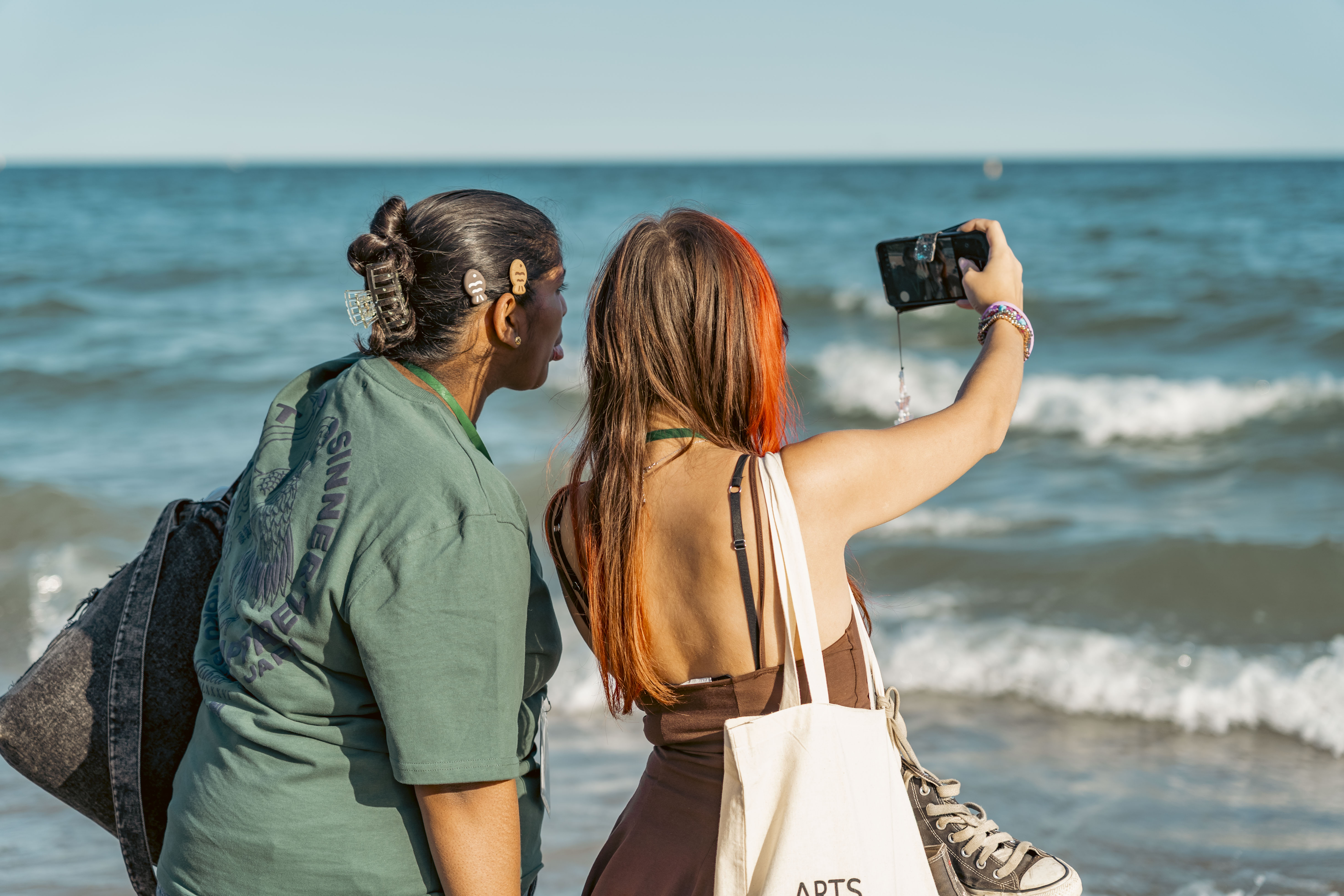 two young females taking a selfie on the beach with the sea in front of them