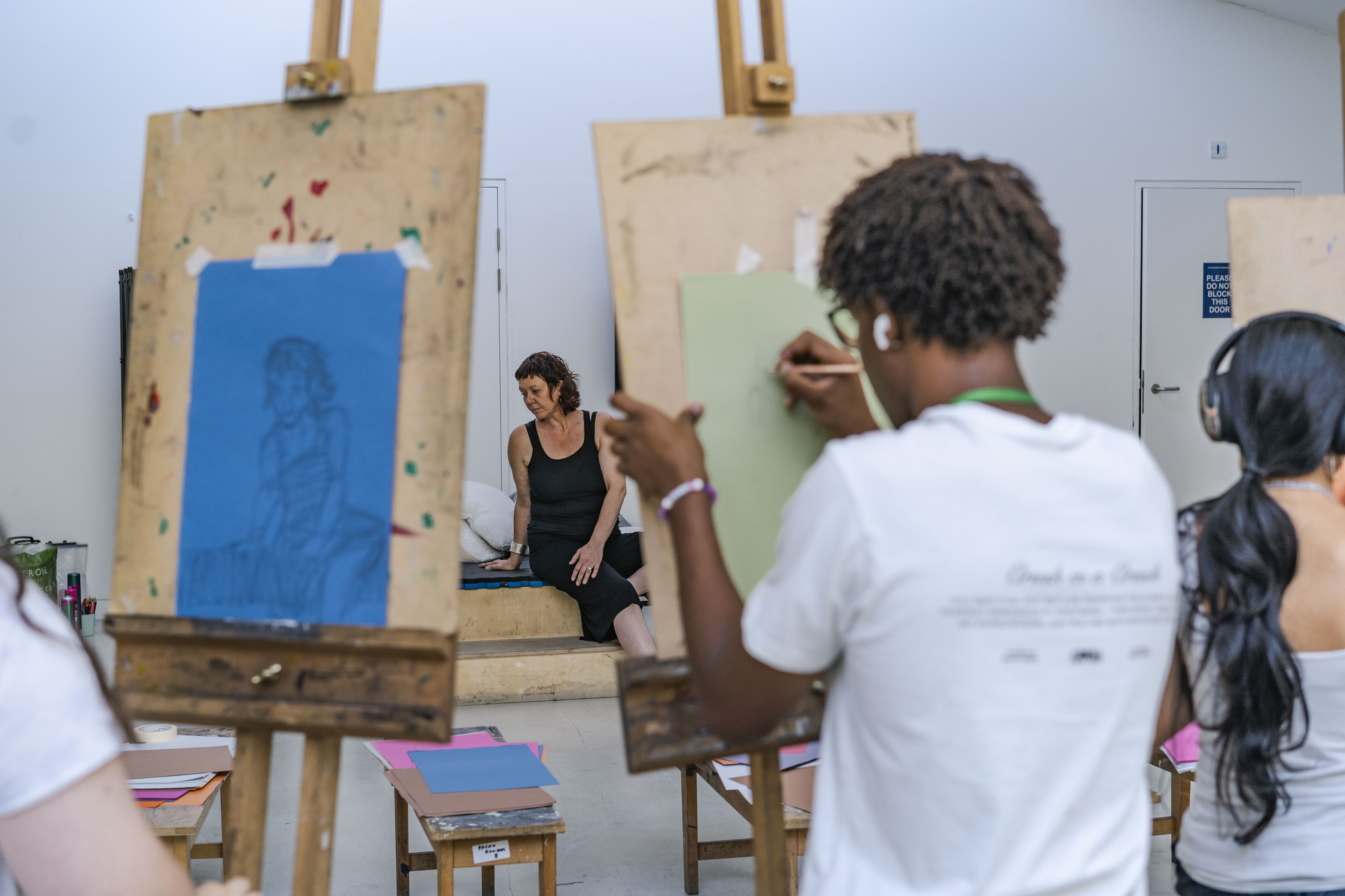 group of students drawing a live model in a sitting position using easel and graphite pencils