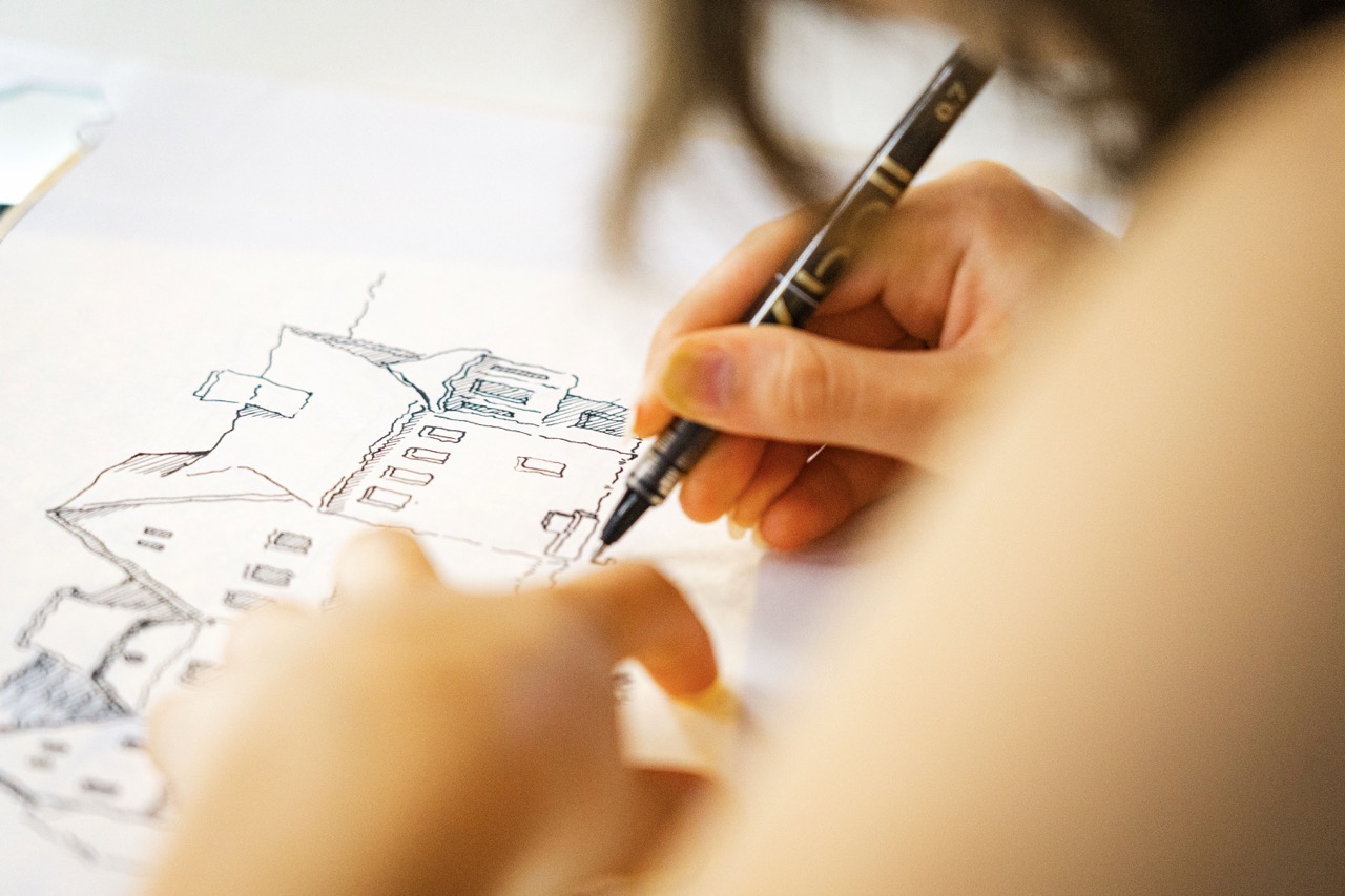 A person sketching a house floor plan with a pencil on white paper, with the drawing filling most of the frame.