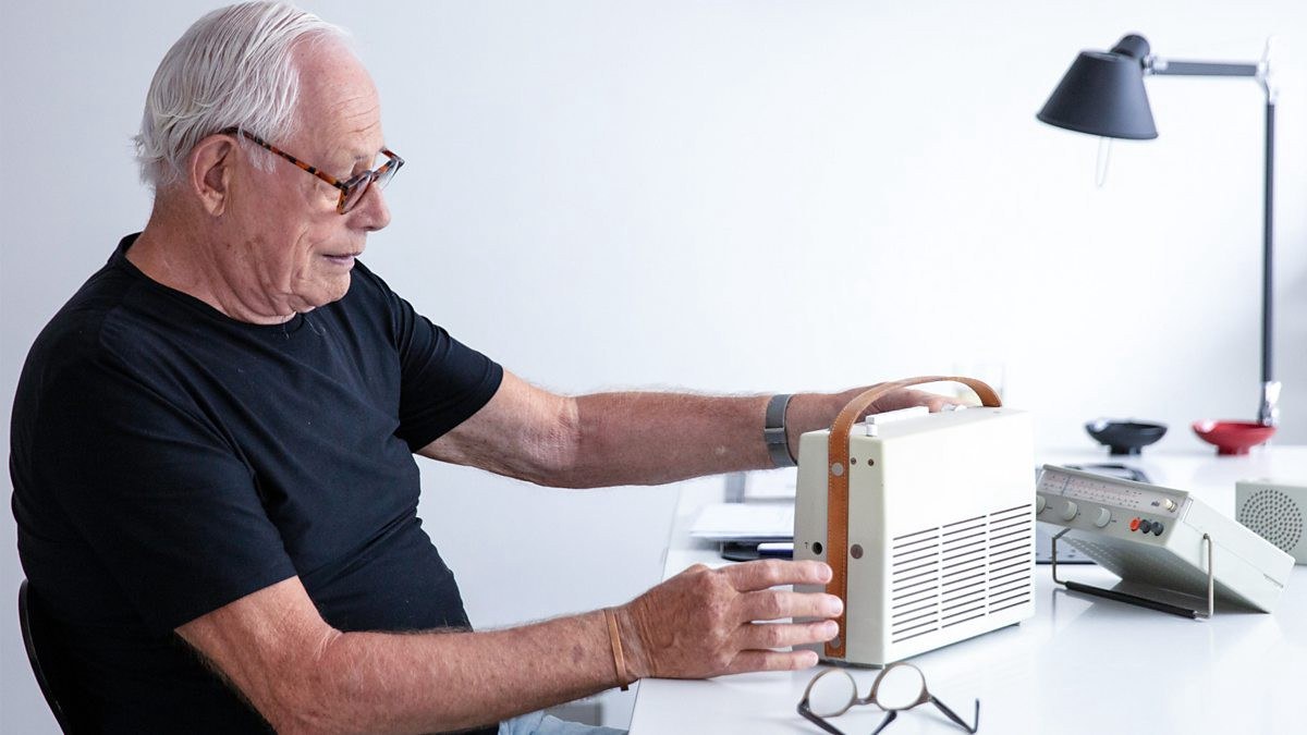 A man sits at a desk and studies a small mobile radio.