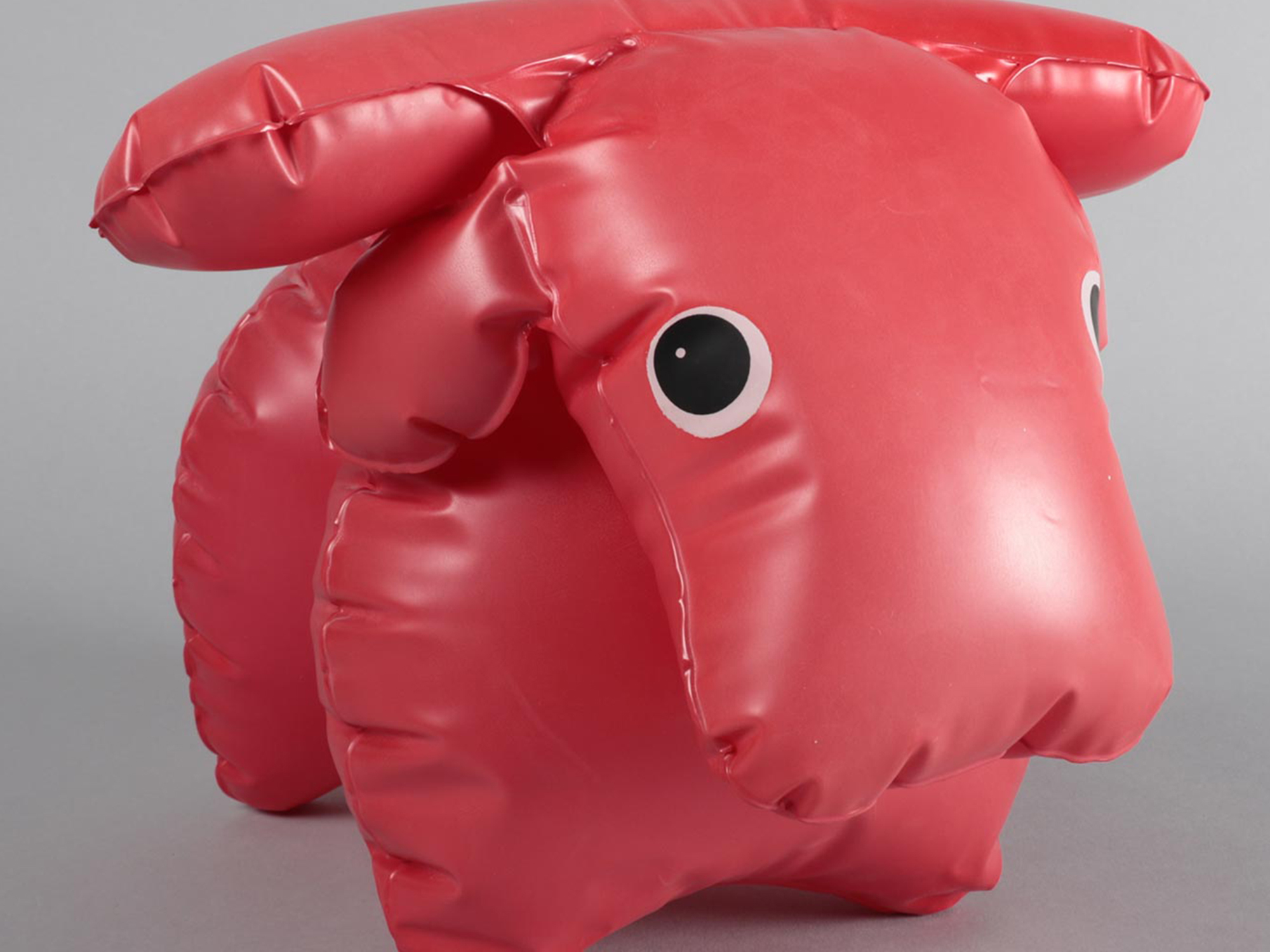 Inflatable pink plastic cow toy standing on a plain surface.