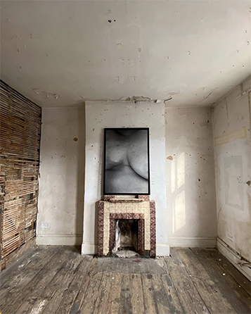 Photograph of a bare room with a fireplace and greyscale photograph of the body