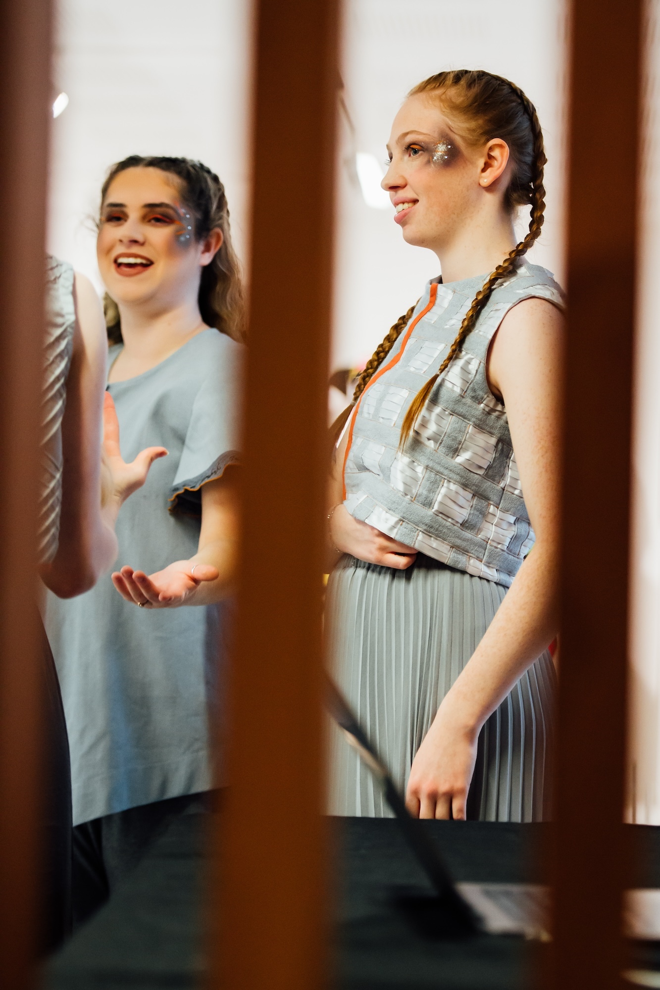 Two BA (Hons) Dance students, pictured through wooden slats in the foreground, laughing and smiling during a performance at TheGallery, Arts University Bournemouth.