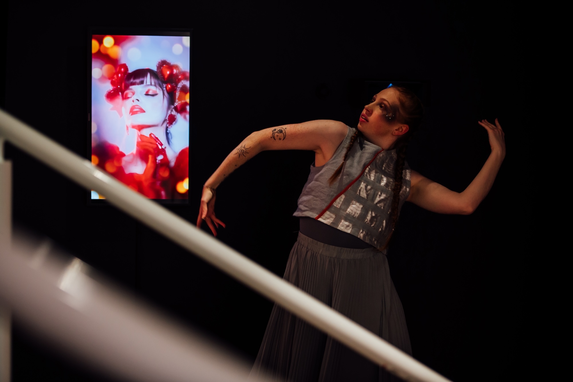 An Arts University Bournemouth student dancer posing during a performance at TheGallery, with a piece of AI generated artwork in the background.
