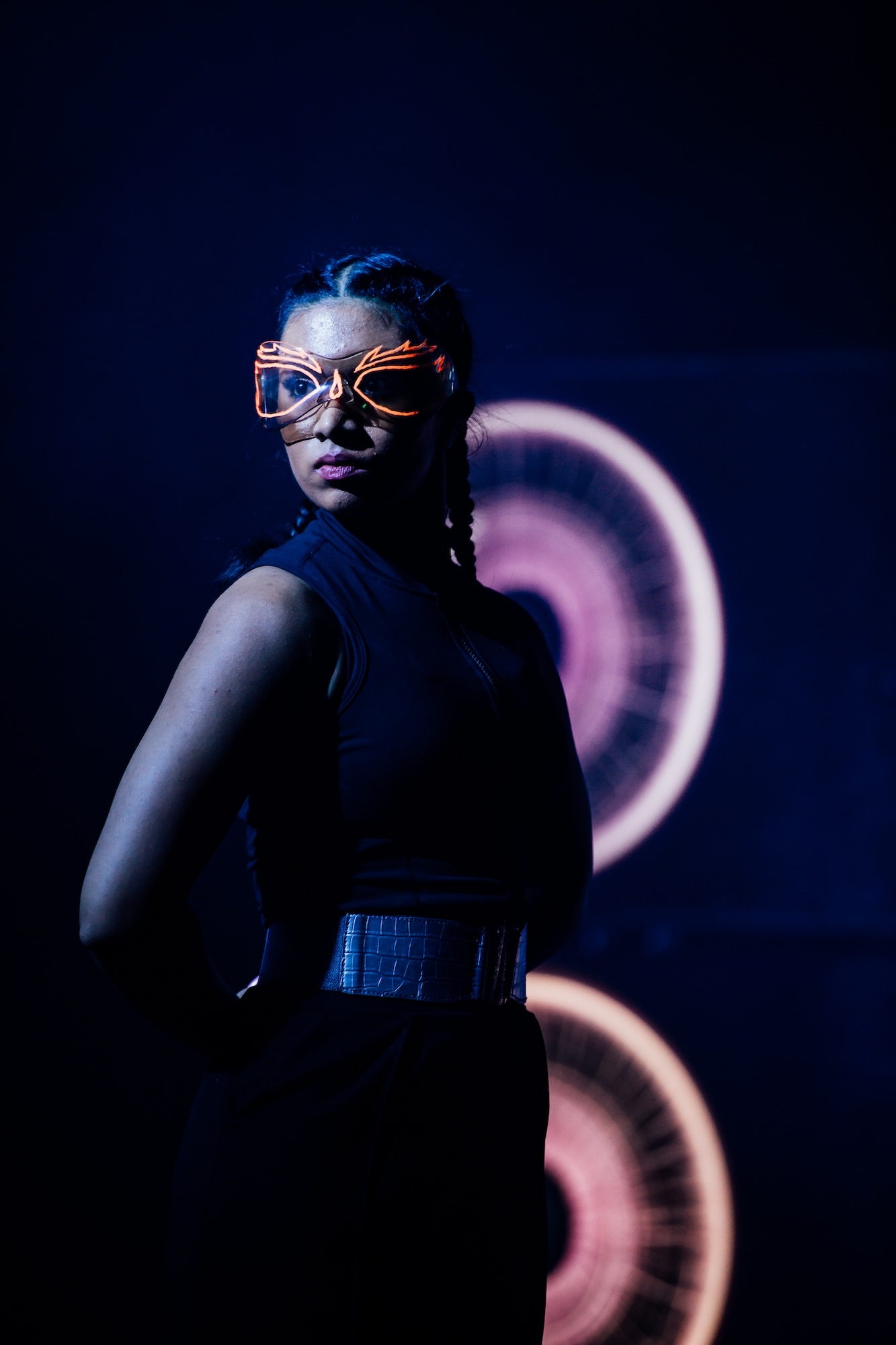 An Arts University Bournemouth student performer wearing large goggles with bright orange accents, mid-performance with a serious expression on their face.