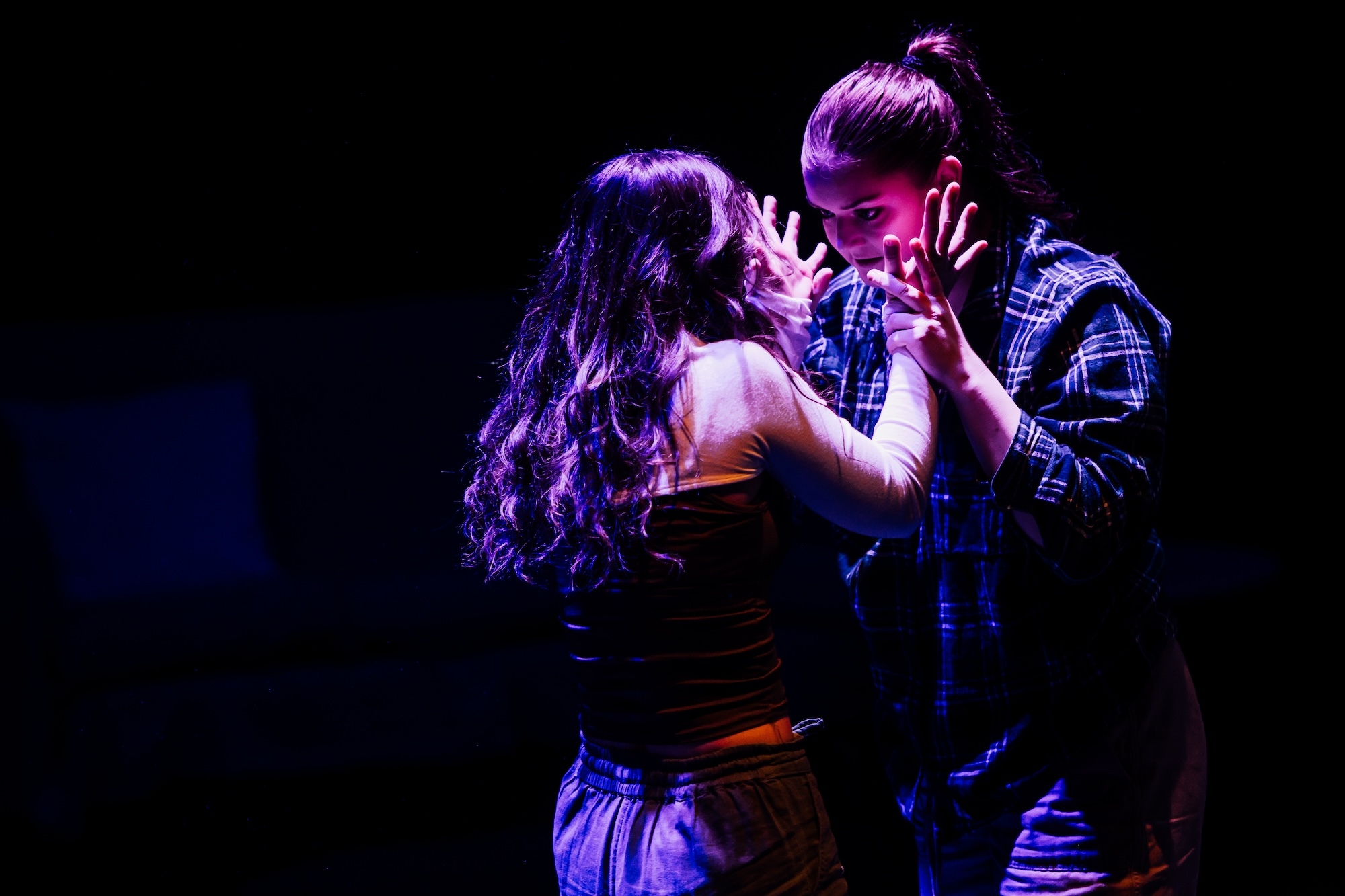 Two Arts University Bournemouth student performers in the middle of a performance. Both performers are standing close to one another, one is holding the other's wrists.