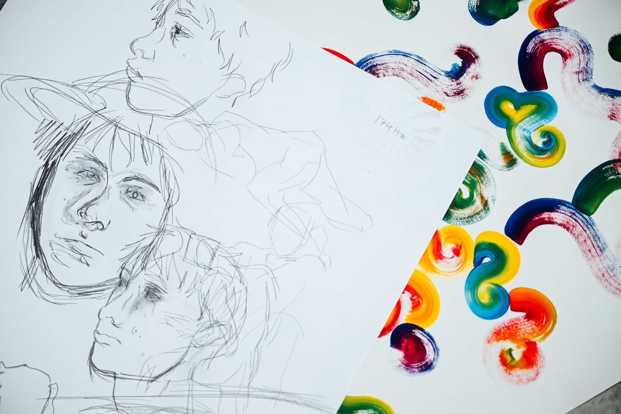Pencil sketches of faces on left side, colourful paint swirls and circles in red, blue, green, yellow on right side of white paper