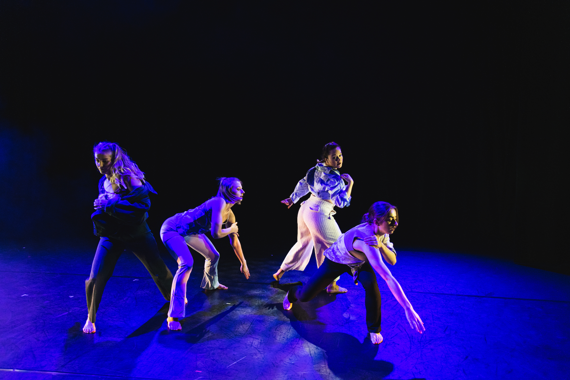 Four dancers in the middle of a routine on a darkened stage.