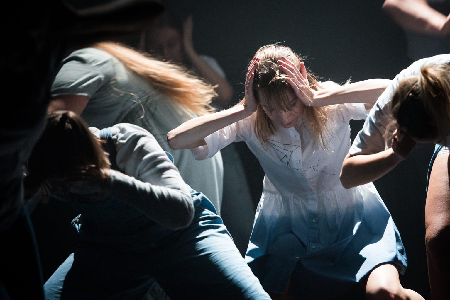 A group of performers in the middle of a performance with their hands on their heads.