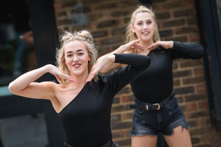 Two dancers in the middle of a routine hold their hands up towards their faces.