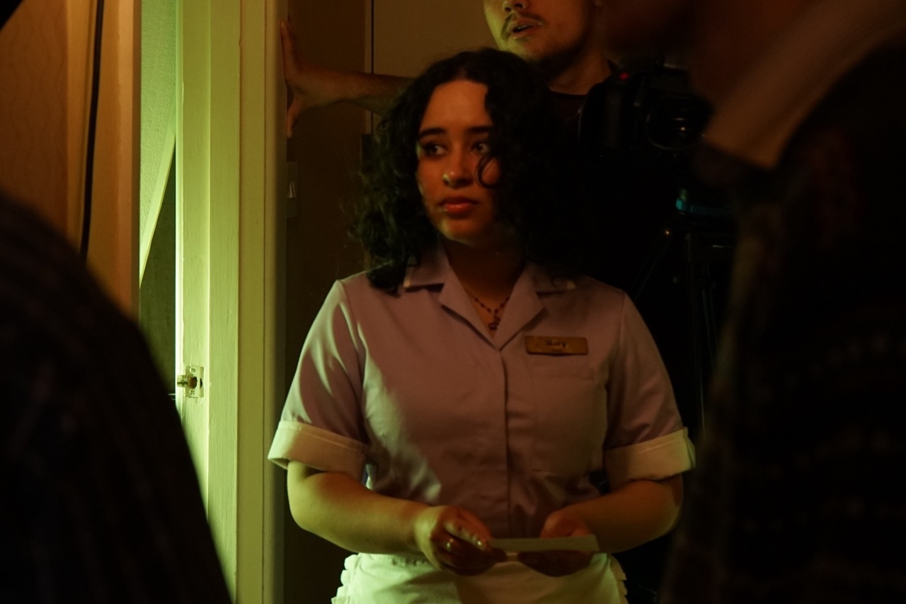 Kasandra Marie Georgi wearing uniform with film crew behind, dimly-lit hallway.