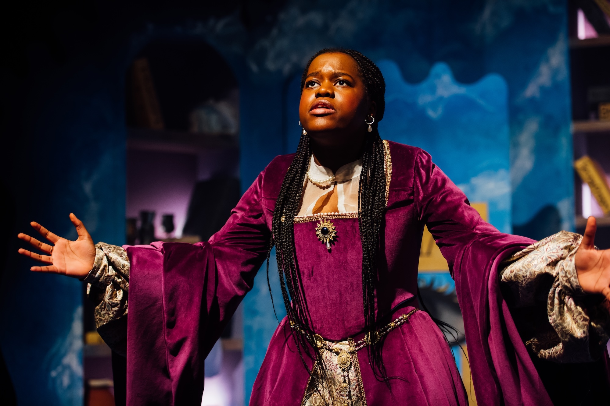 An actor in a pink 17th Century dress on stage.