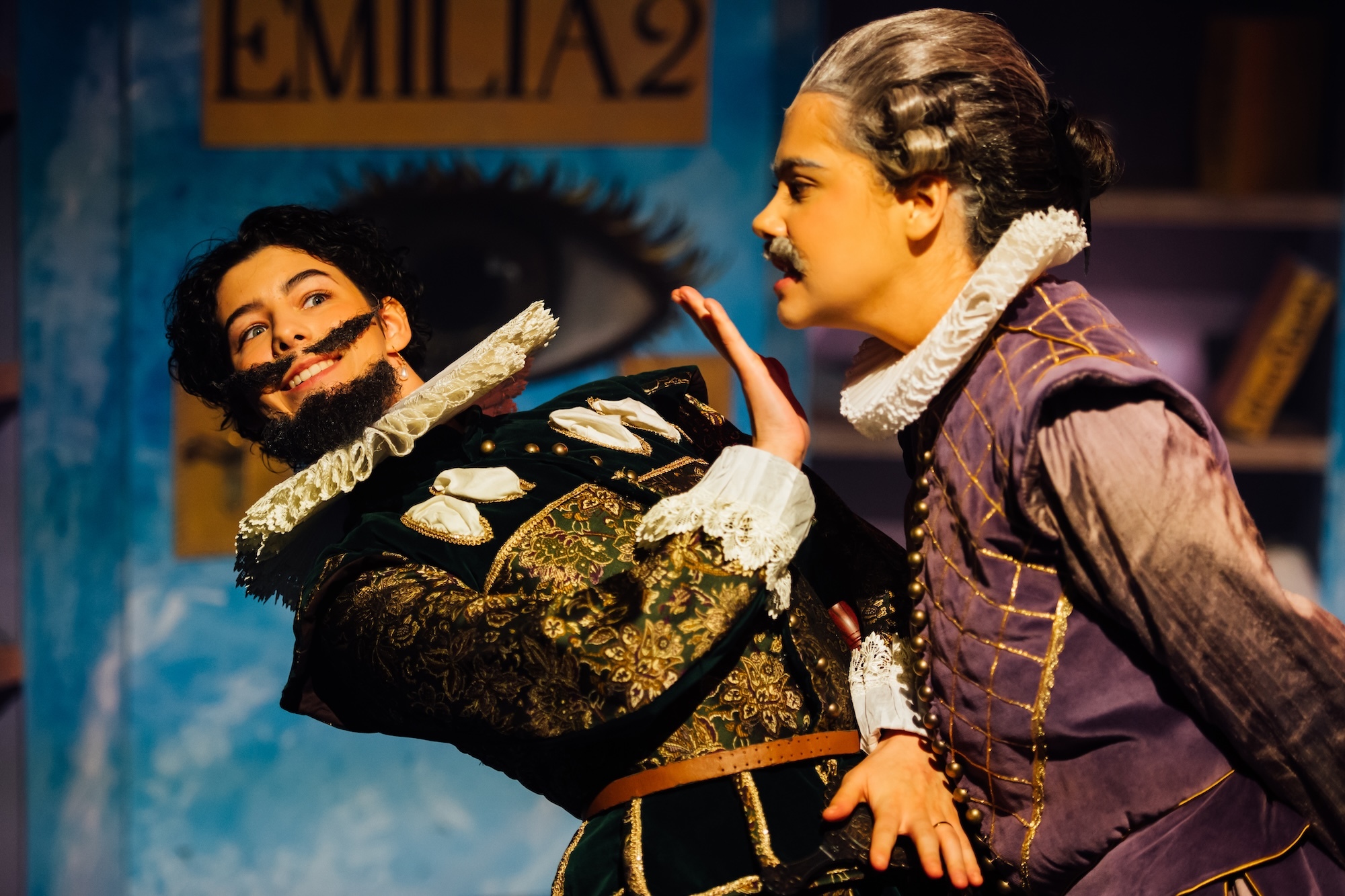 Two actors on stage in 17th Century garments, one leaning away from the other.