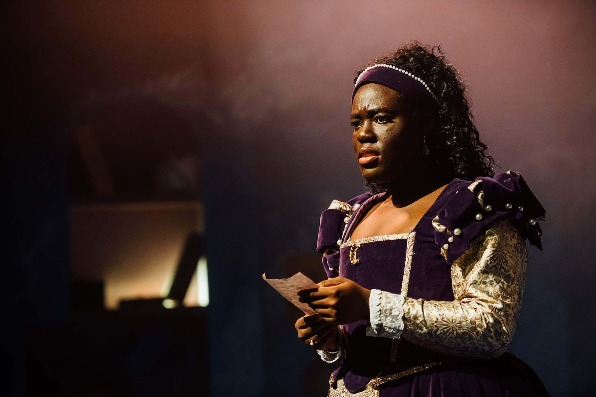 A BA (Hons) Acting student under stage lighting in a purple 17th Century garment.