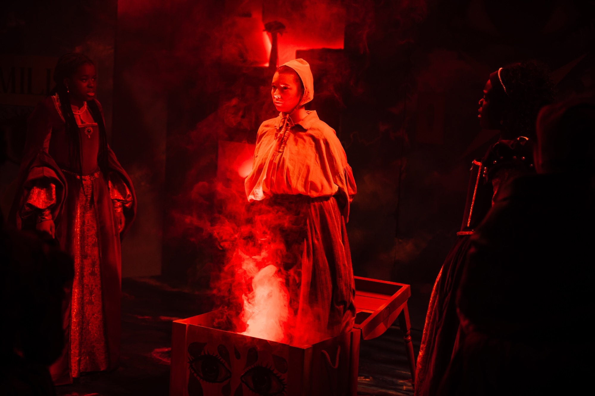 An actor emerging from red smoke on stage wearing 17th Century clothing.