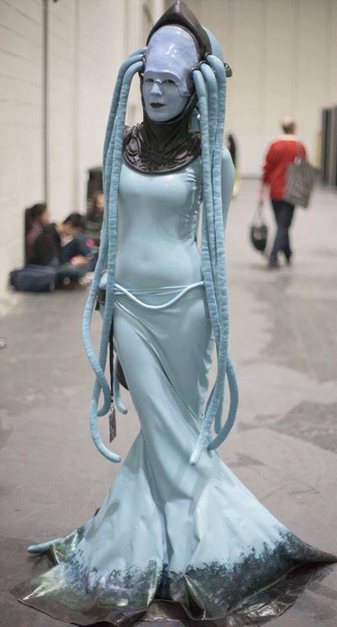 Dora Voros wearing a long, flowing light blue dress with alien tentacles.
