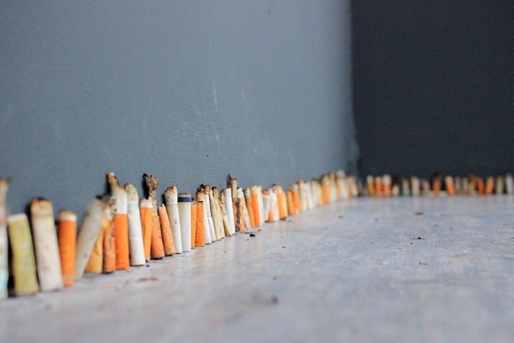 A large number of used cigarette butts lined up along a background and around a corner.