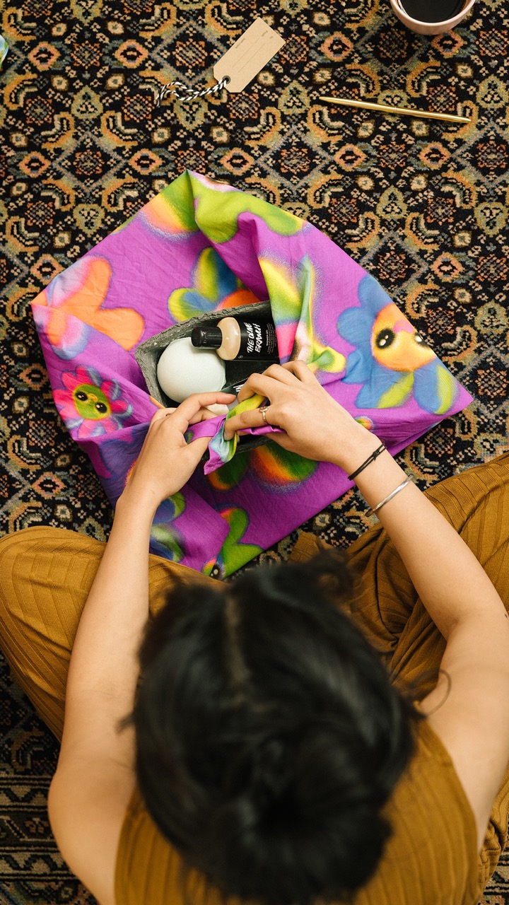 Person folding up a colourful purple knot wrap with flowers on it, down-facing shot, brown carpet.