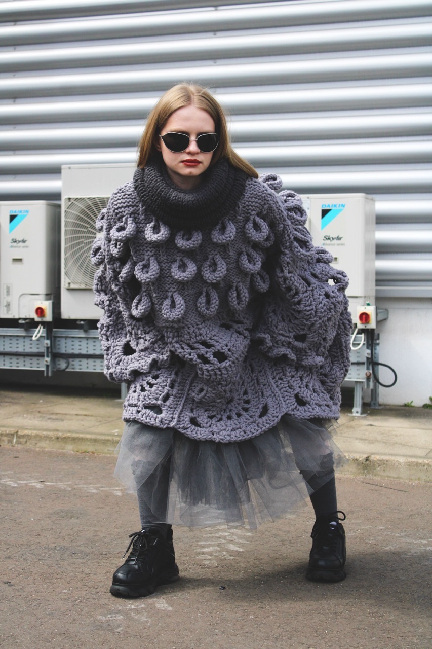 Model wearing a large grey crochet piece outside.