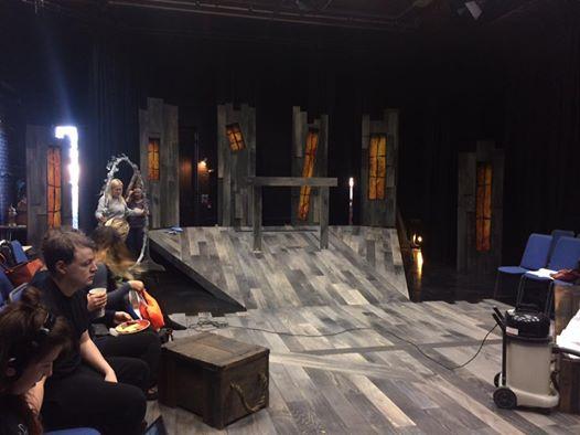 A sloped stage set with windows at the end, and people sitting to the left.