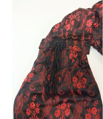 Early 1900s-style silk damask bodice, floral red and black pattern with cream ruffles, white background, sleeve detail.