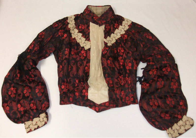Early 1900s-style silk damask bodice, floral red and black pattern with cream ruffles, white background.