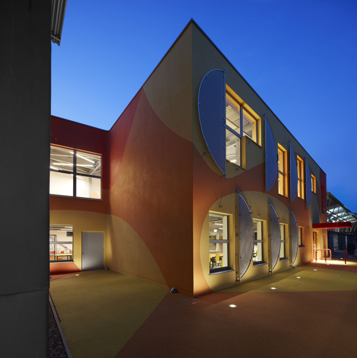 Innovation Studio, photographed by Richard Bryant. The exterior of the building is shown at dusk, with light shining through all windows.