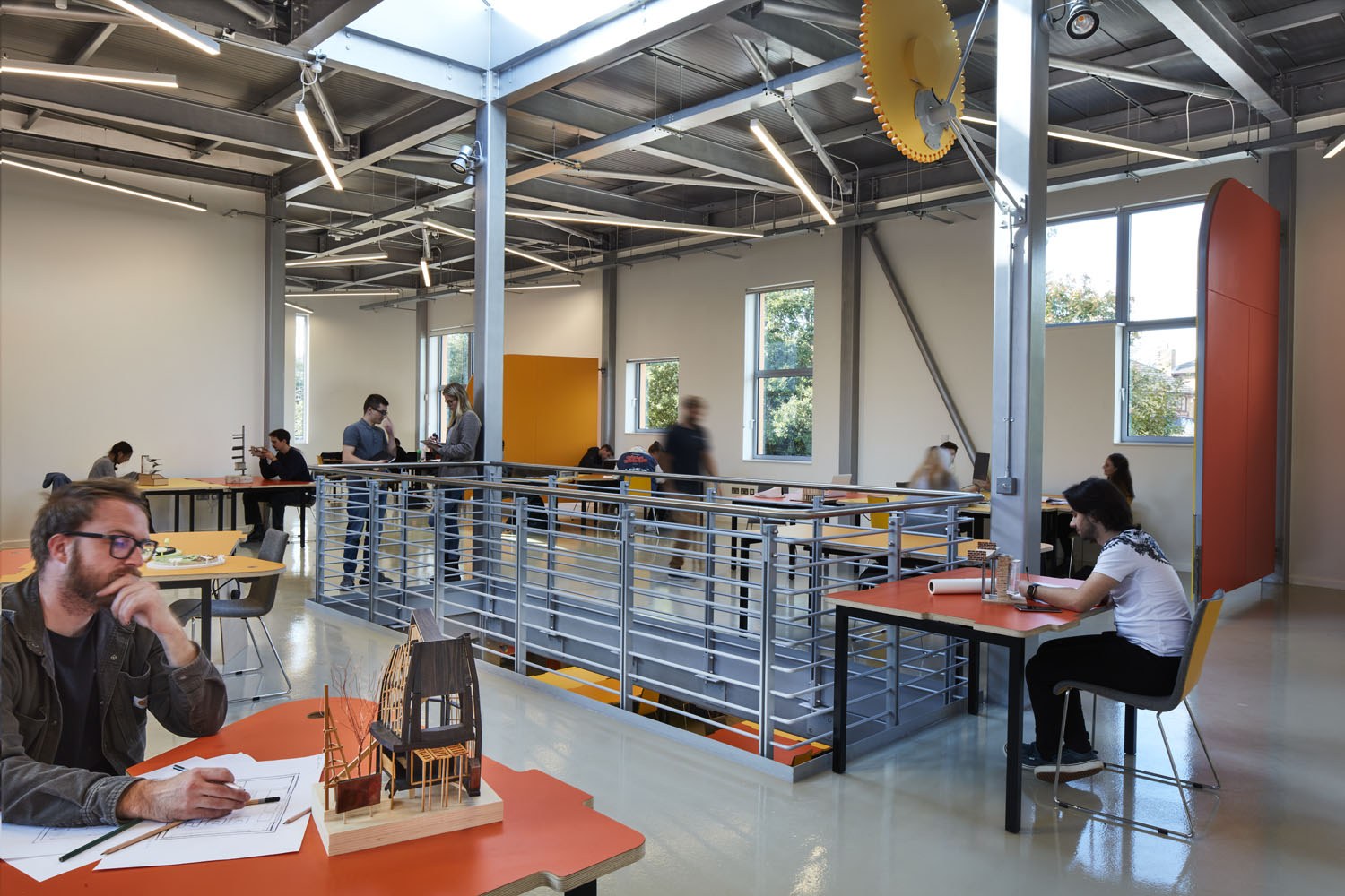 Innovation Studio, photographed by Richard Bryant. Photo of an interior space, with several people sat working at tables. A rectangle-shaped railing is in the middle of the room.