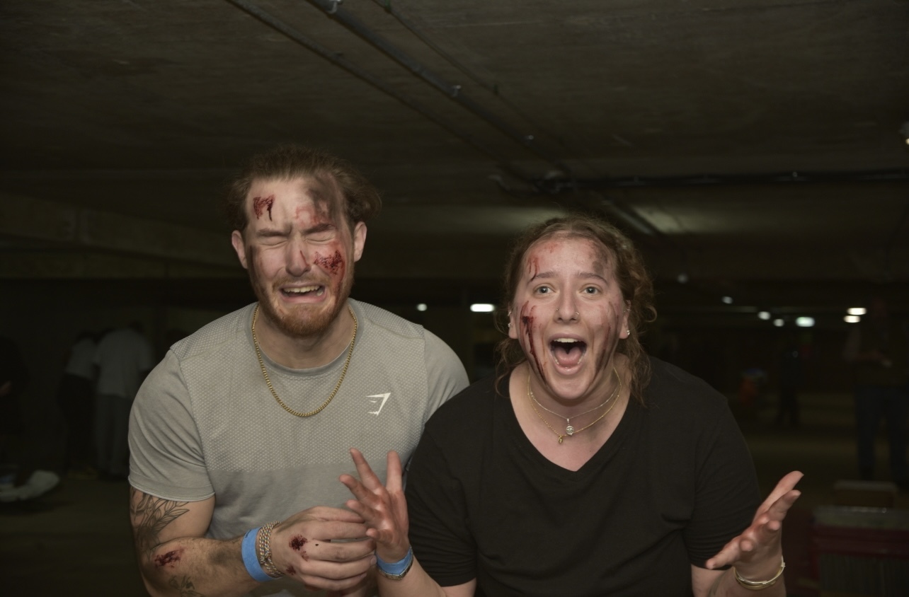 Two models covered in fake injuries, acting in distress, dim car park background.
