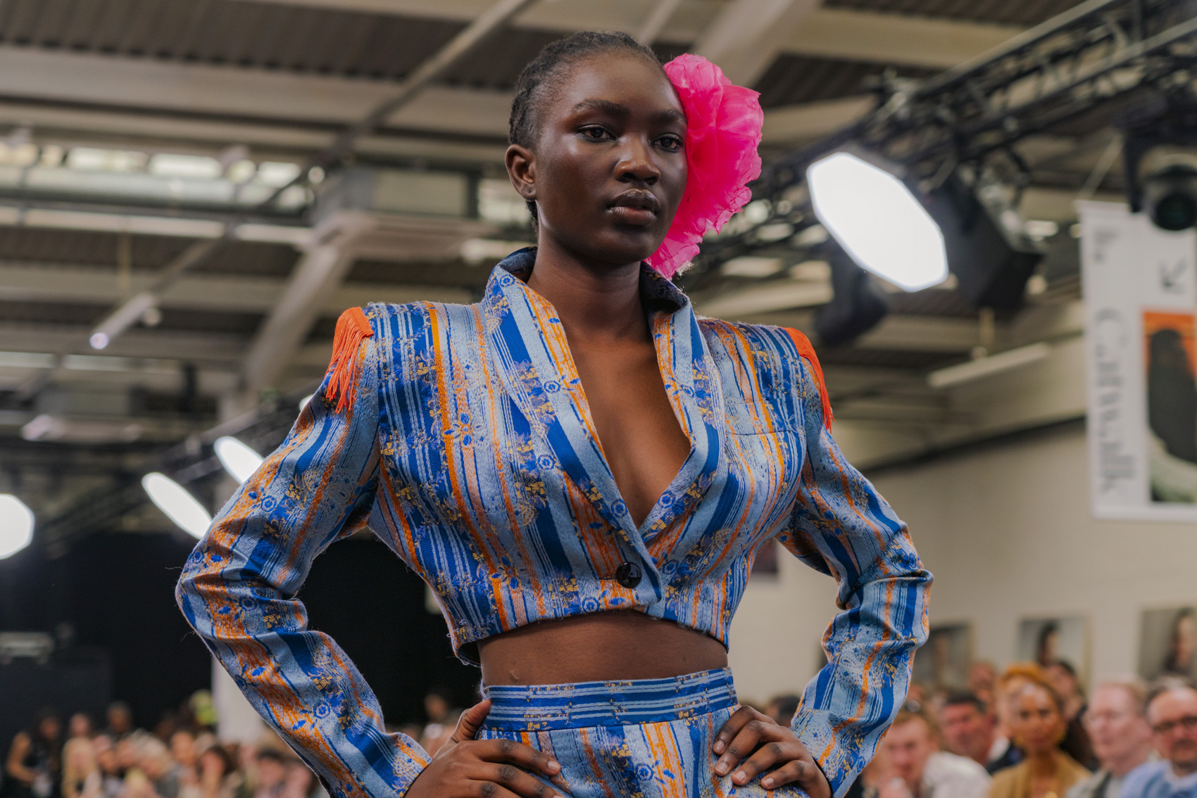 Model wearing vibrant blue and red striped floral garment, bright pink headpiece.