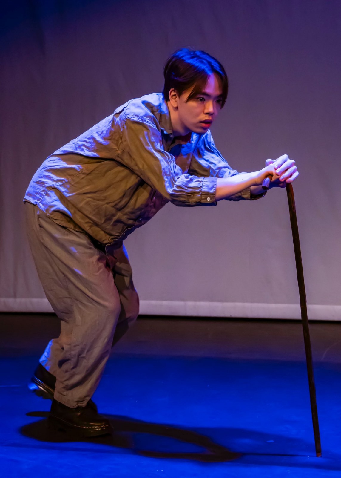 Mitsuki Kawase on-stage under blue lighting, hunched over with a walking stick.