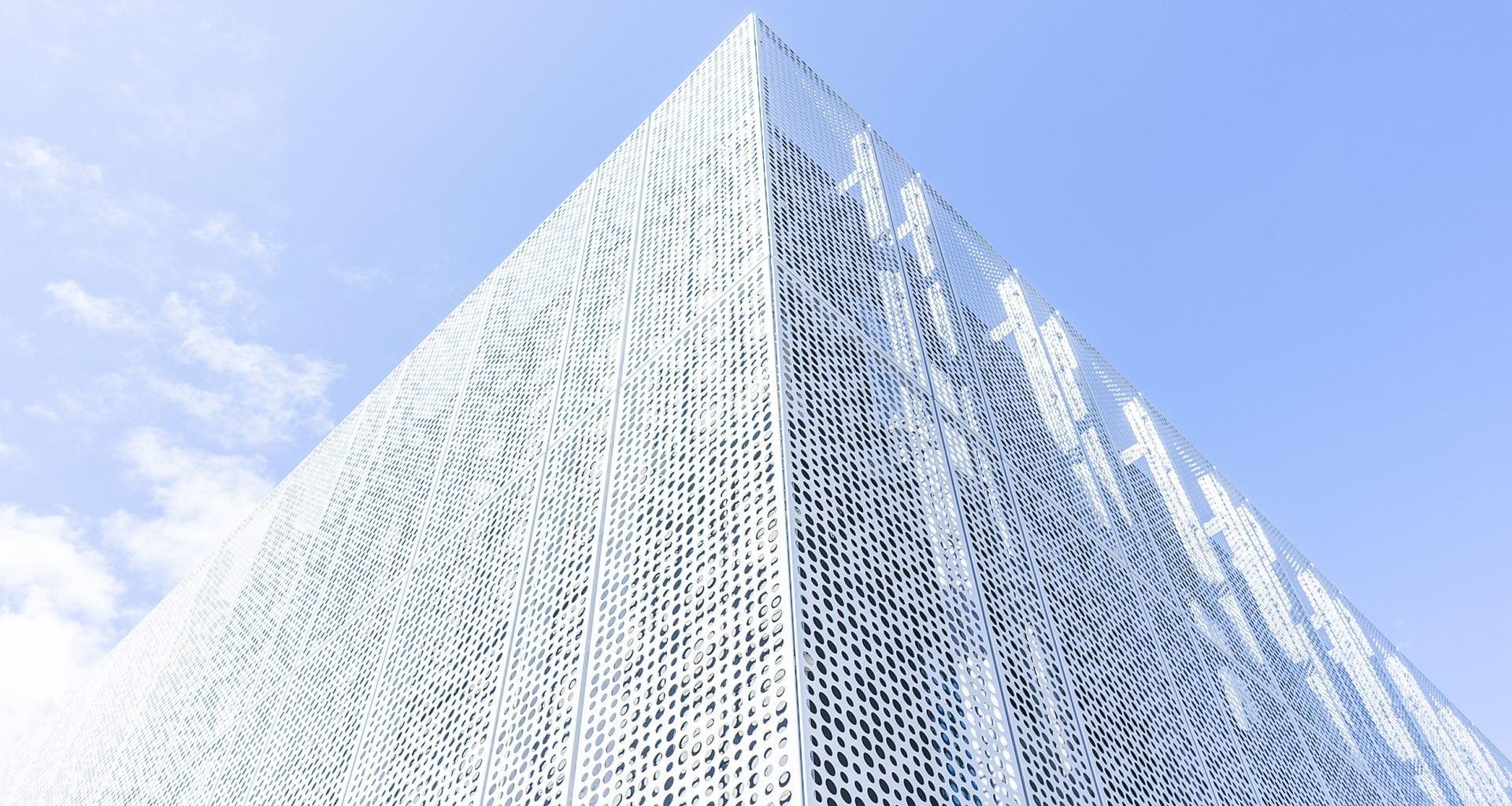 An abstract view of a building on campus – two sides of a building meeting to make a point in the middle. The material is grey metal with lots of holes cut out.