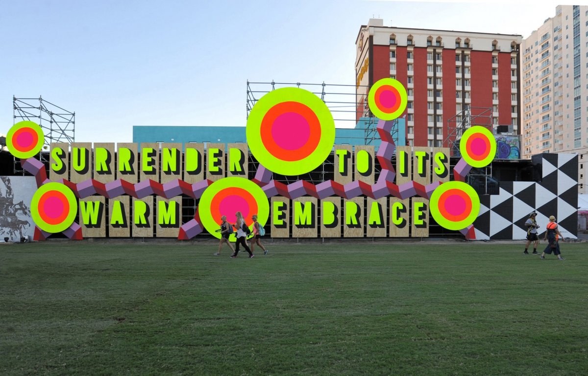 An artwork structure made up of brightly coloured circles and blocks with letters making the words 'Surrender to its warm embrace'.