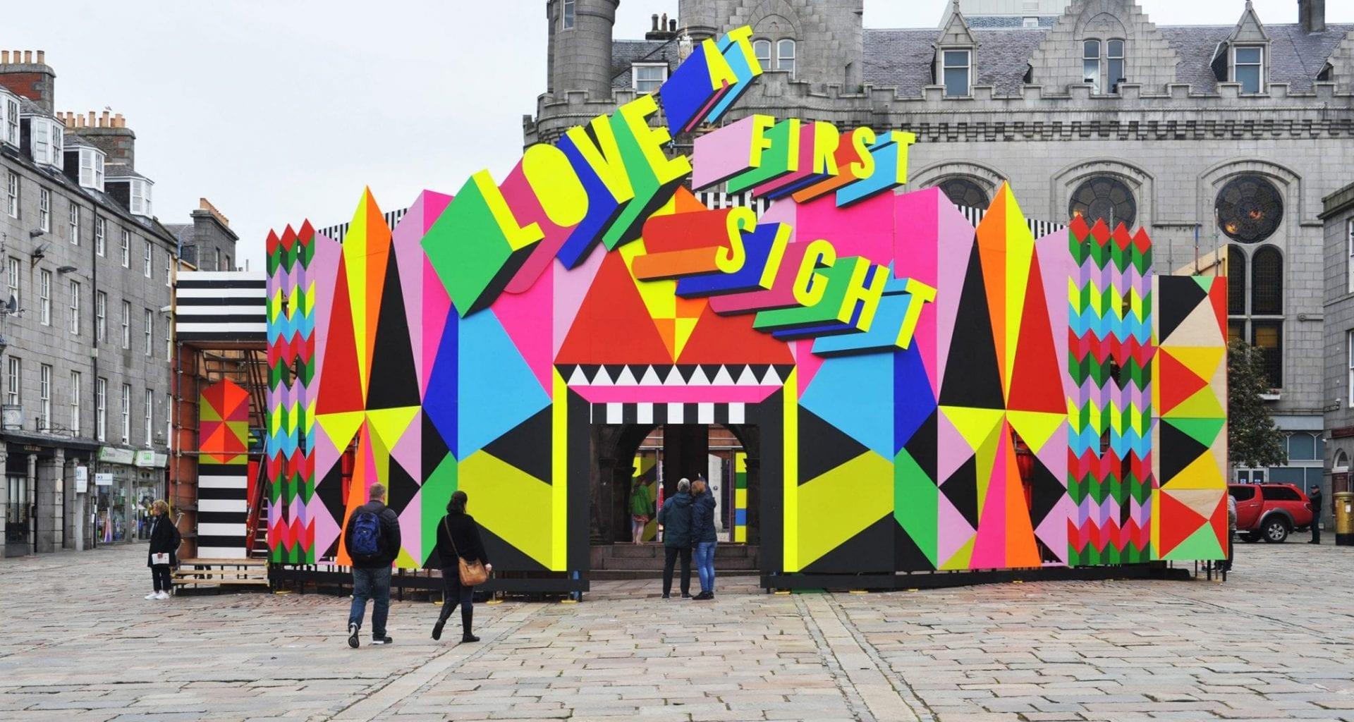 Pop-up building set up on a high street. The building is decorated with colourful block shapes and has the words 'Love at First Sight' appear above the front entrance.