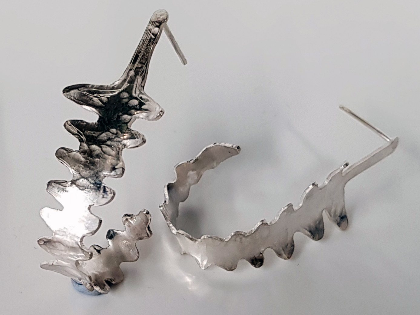 Pair of silver earrings with jagged and curved shapes.