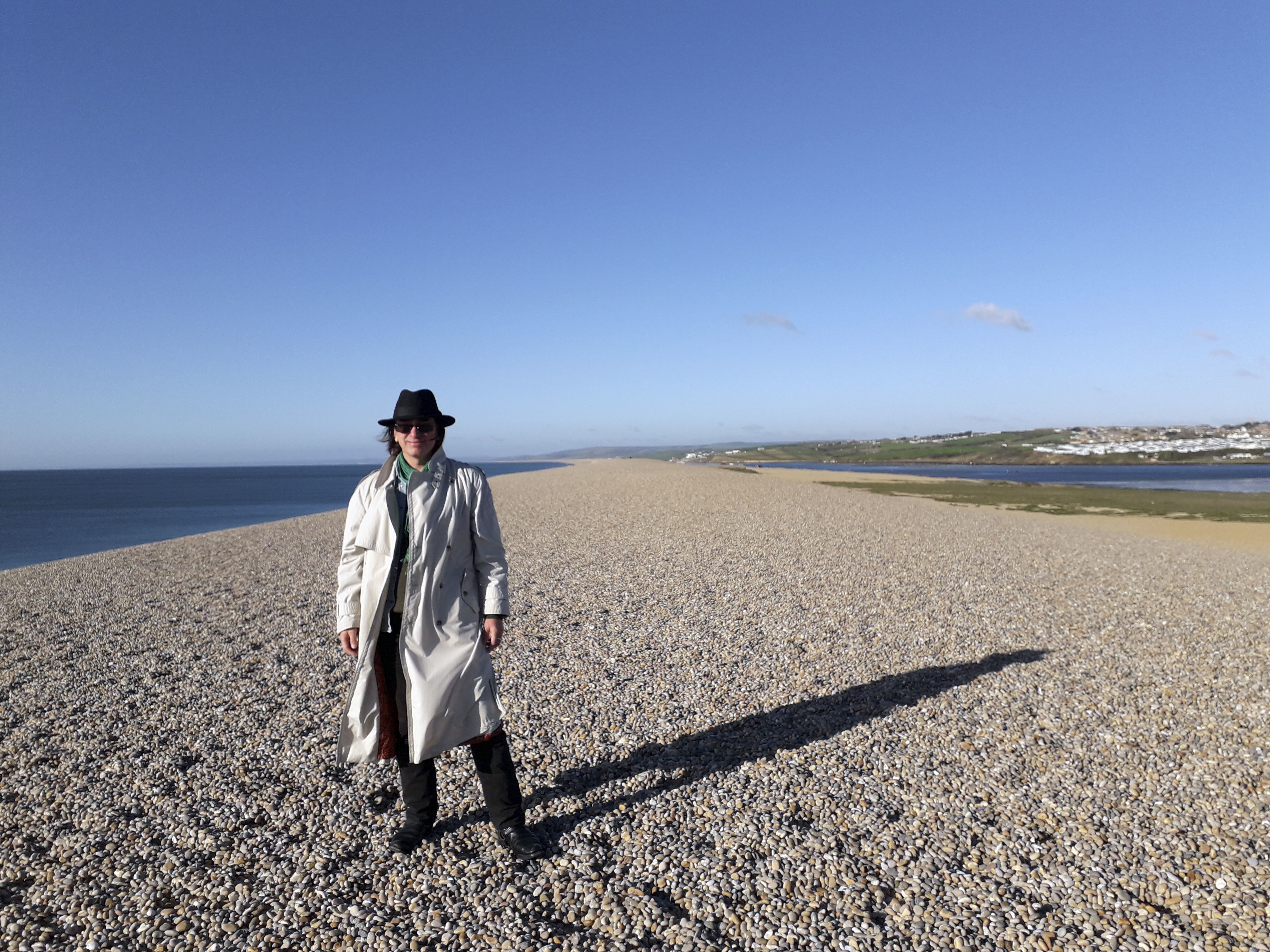 Dr Kevan Manwaring, Senior Lecturer in Creative Writing, standing on a stony stretch of beach.