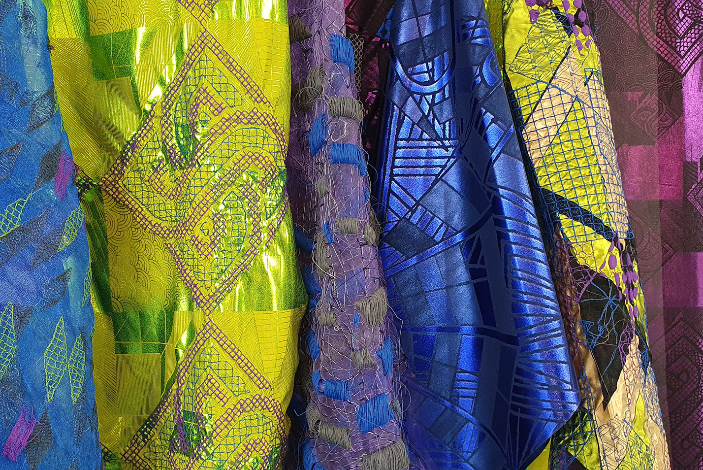 Six lengths of fabric of different patterns and colours hanging next to each other.