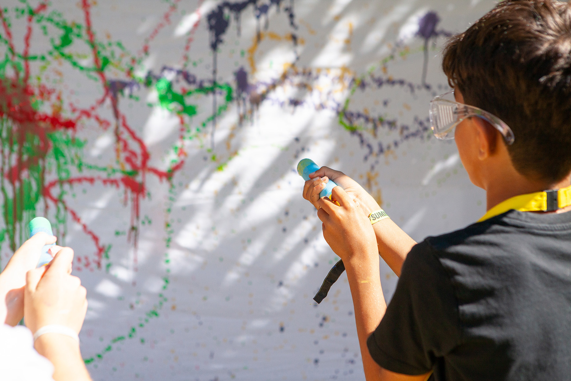 A young student is firing a paint gun at a paint-splattered canvas