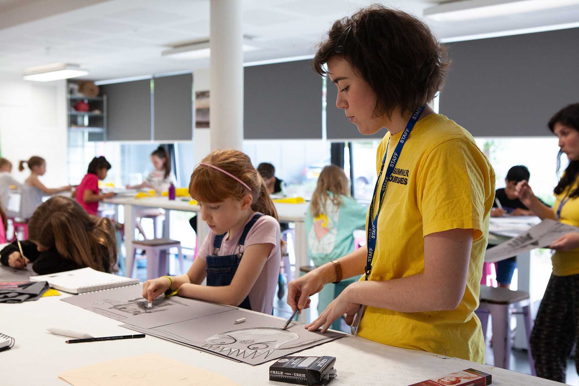 A young student is painting and being helped by a teacher