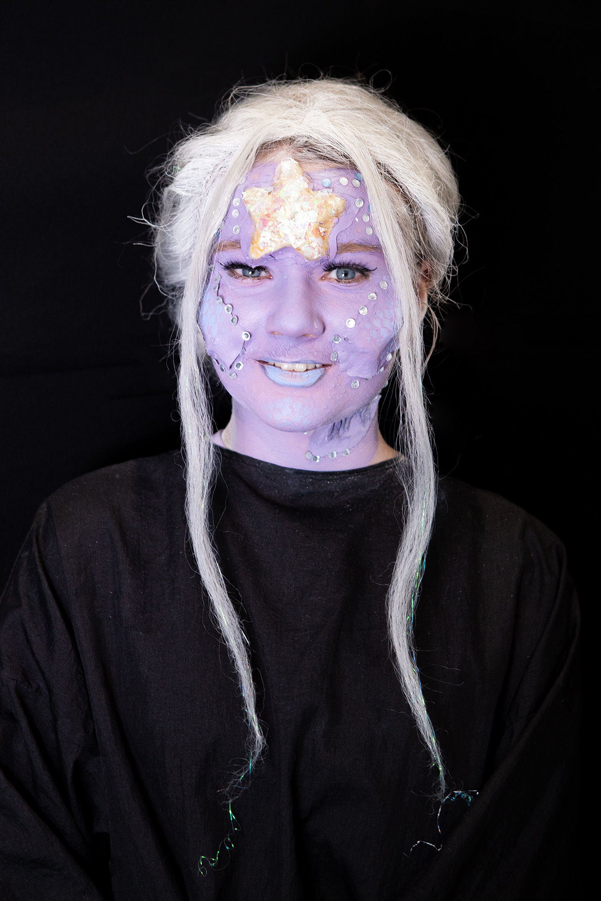 An example of character makeup: a student has their face painted purple with a prosthetic starfish on their forehead