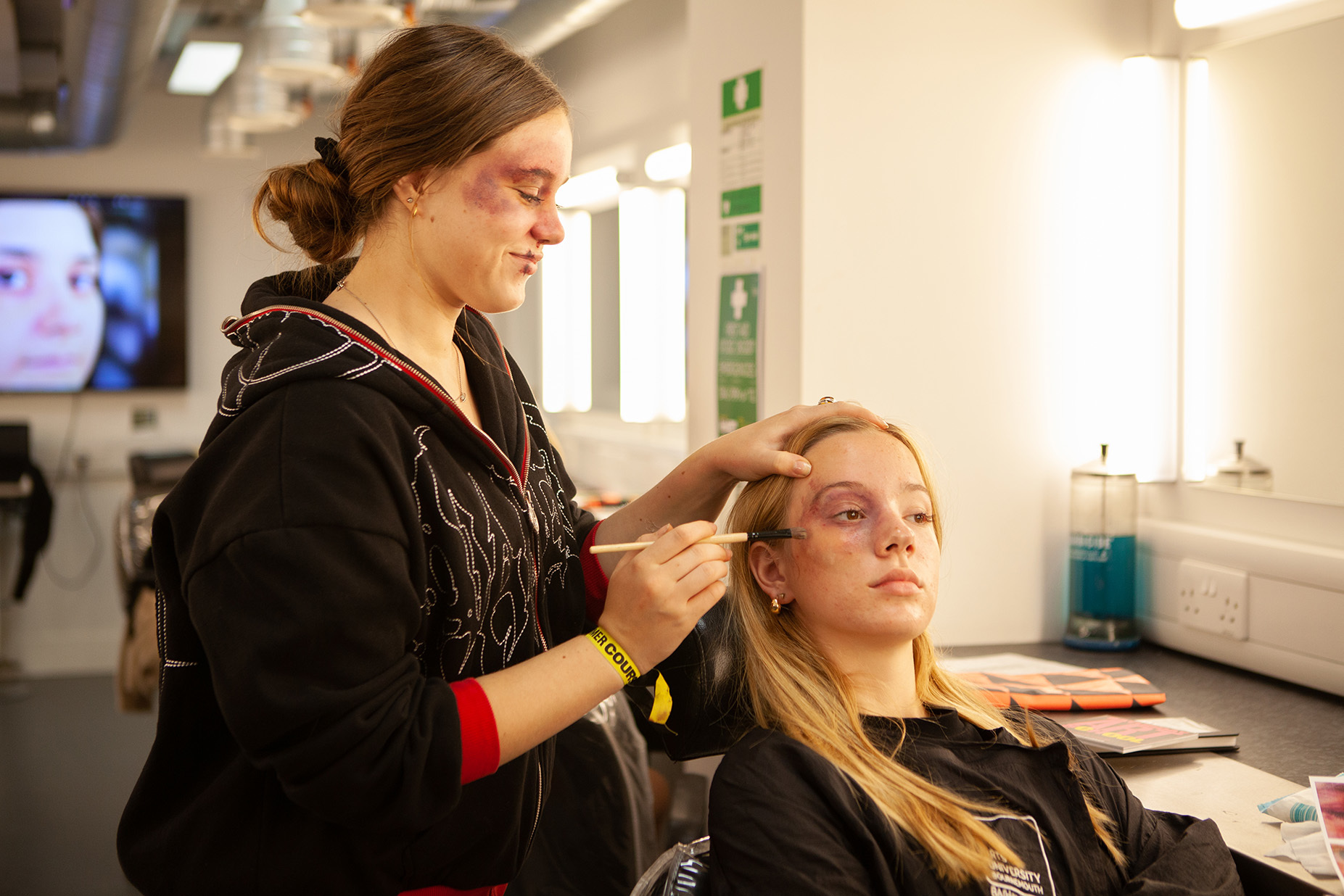 A student is applying makeup to another student's face