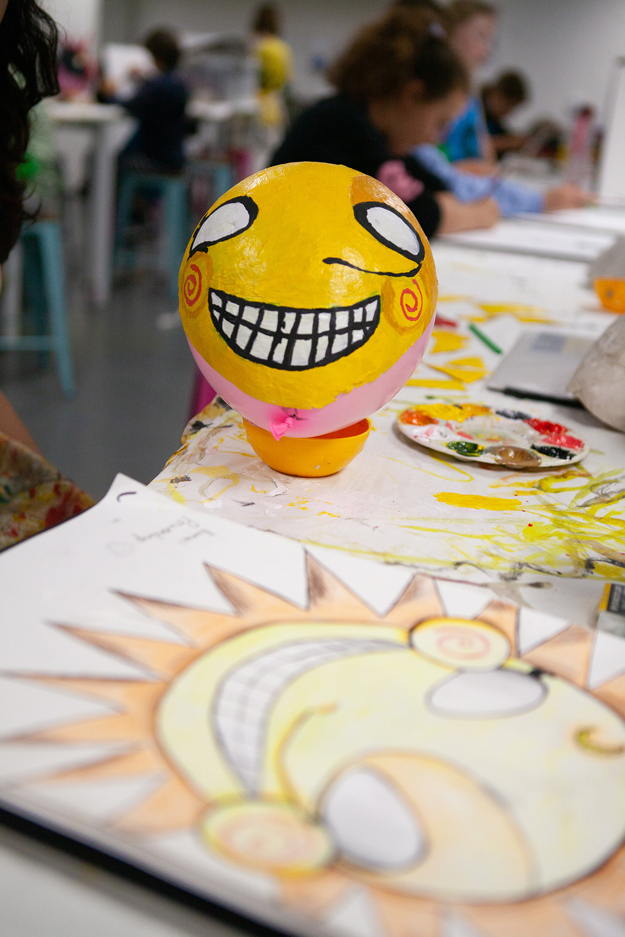 A papier mache sphere with a yellow face painted on it