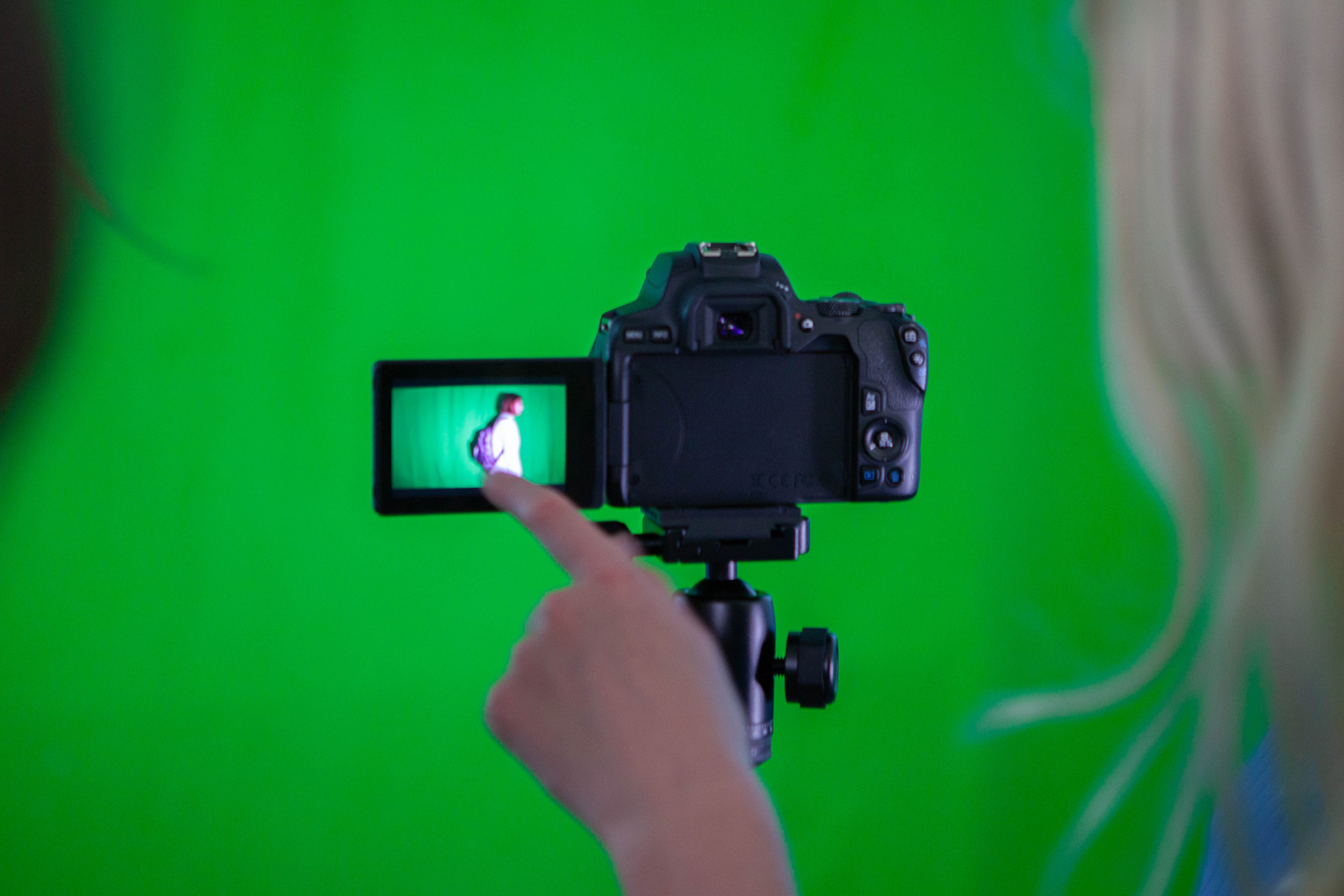 A student is looking at the camera screen. They're in front of a green screen.