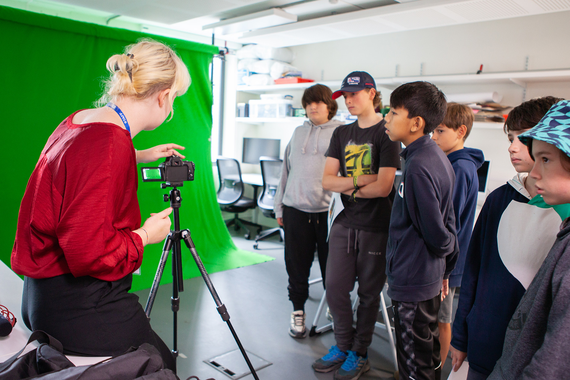 A group of students watches the teacher set up a camera