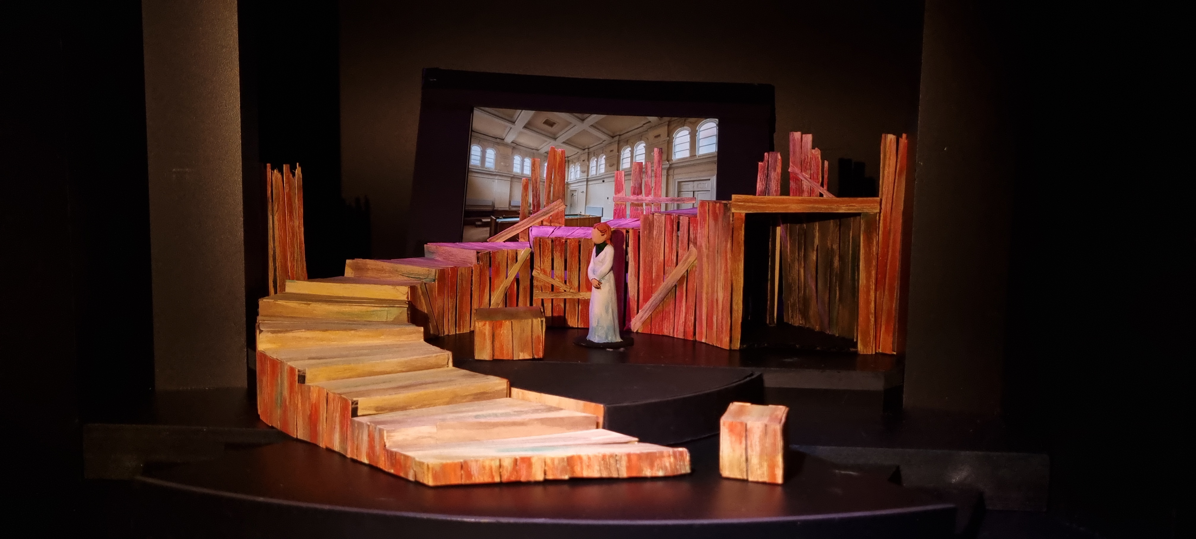 A model stage set with wooden curving stairs and a screen in the background.